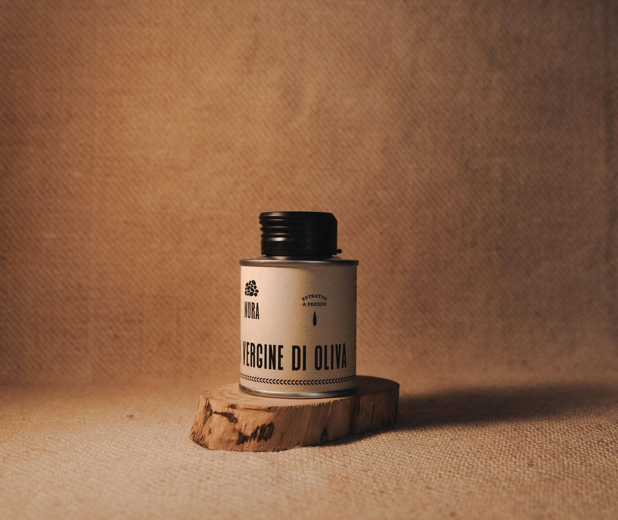 Lattina di olio extravergine Nura con etichetta chiara, su un tronchetto di legno